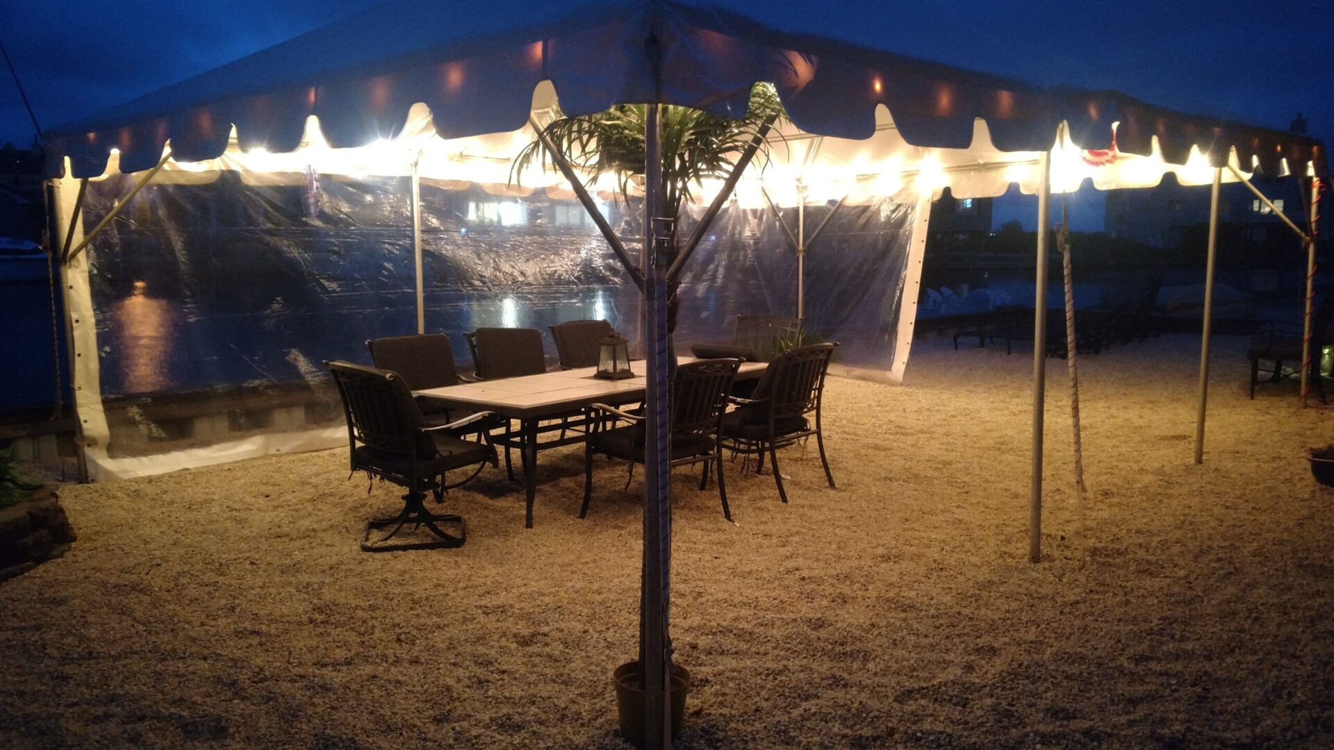 A long table with seven chairs under a white tent with lights