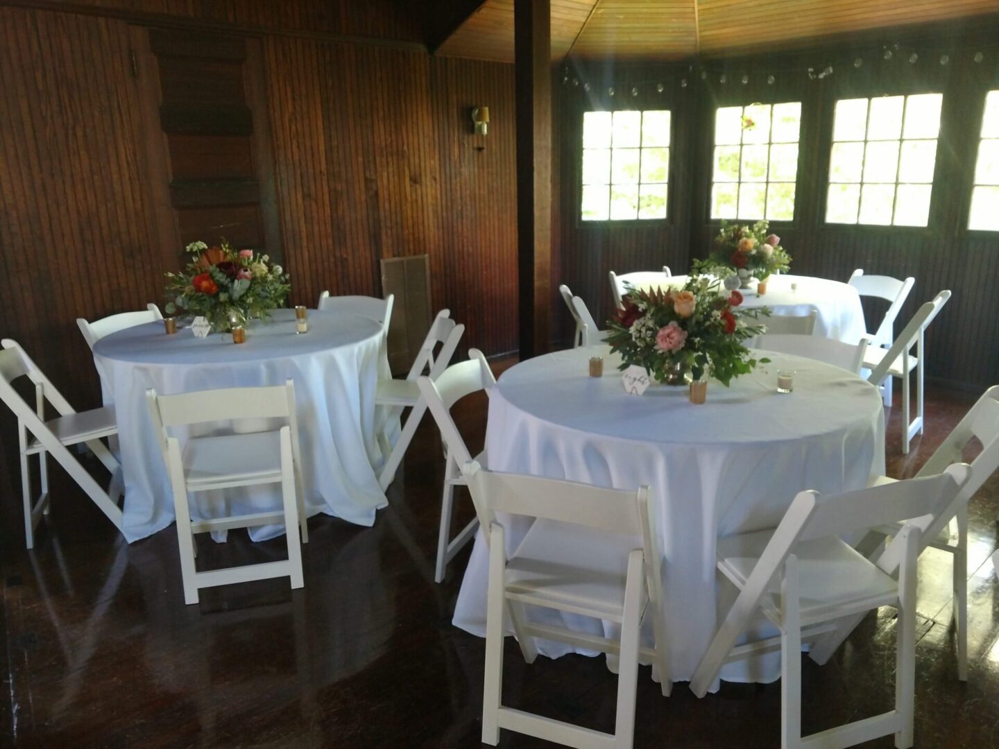 Three round tables with white table cloth and three flower center pieces